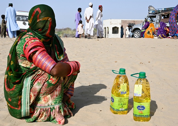 Woman in Pakistan sitting on the ground beside two containers of oil