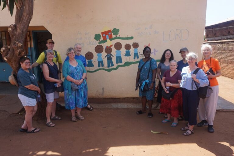 11 Malawi learning tour participants standing in front of a building.
