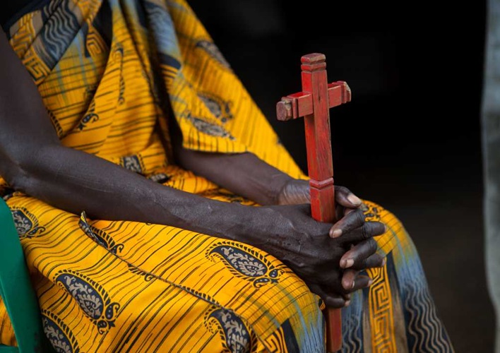 Person sitting holding a wooden cross