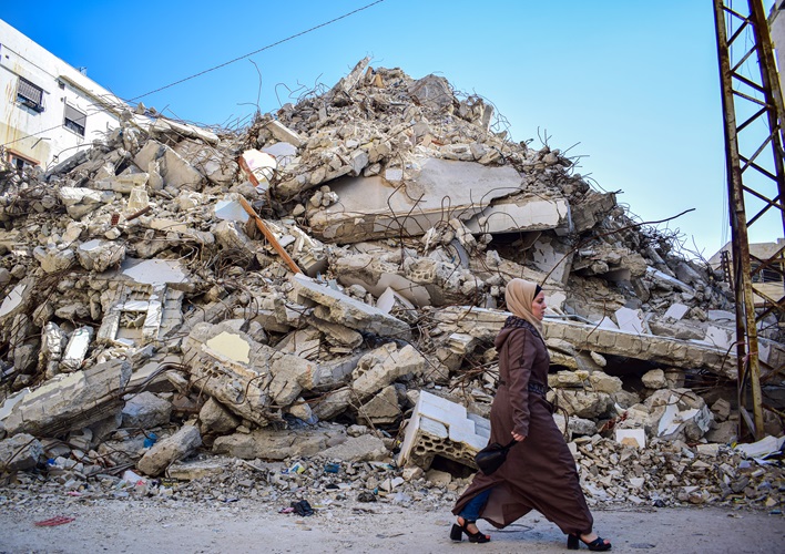 A woman walking in front of a destroyed building.