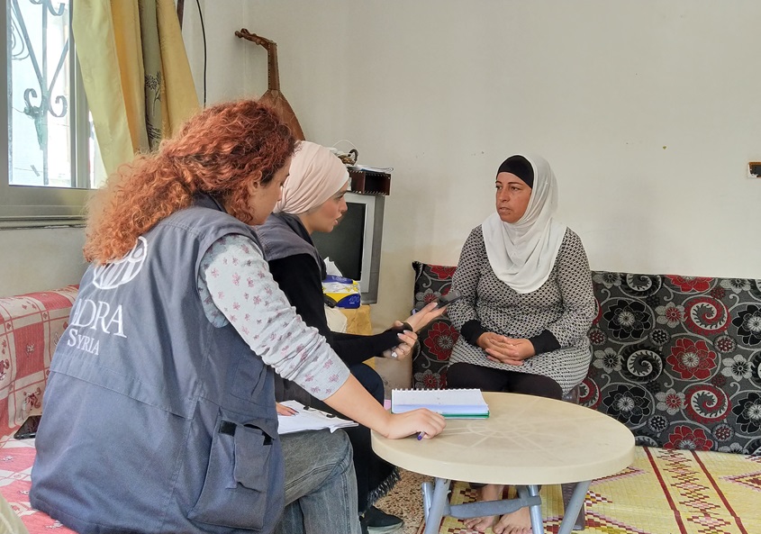 Two workers interviewing a woman in her house.